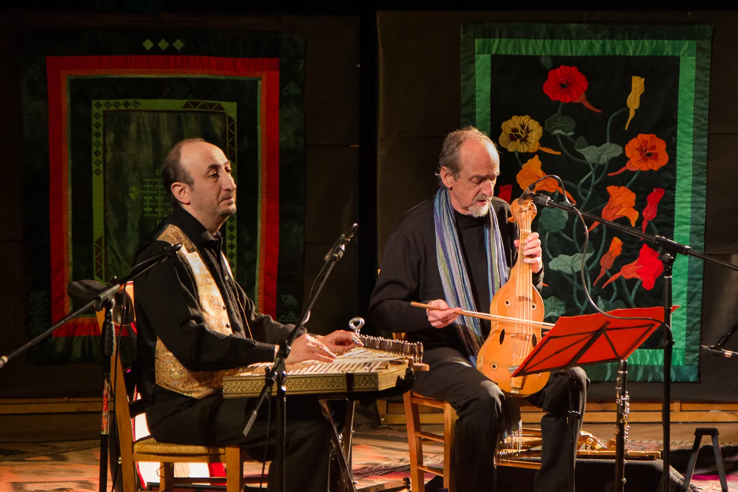 Two seated musicians in front of textile works