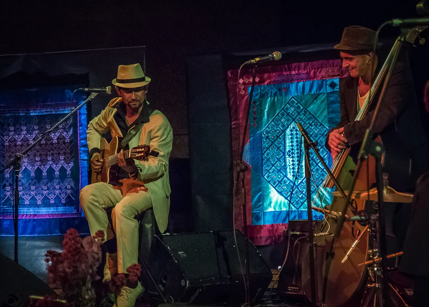 A guitarist and double bassist performing among textile works