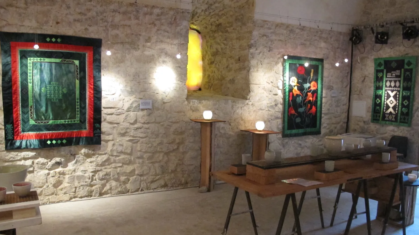 Green and red textile works with ceramics in a stone gallery